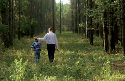 Darren Jackson walks with his son, Bishop, alongside a stand of timber on the family farm.