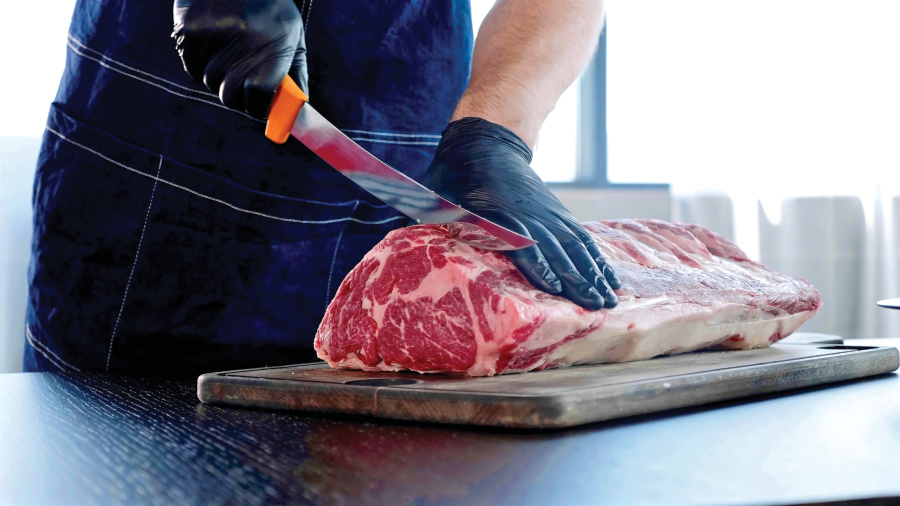 Chef cuts raw meat on the wood board with the knife, close-up. Chopping meat for cooking steak at reastaurant.