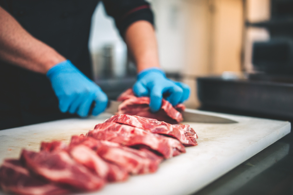 closeup view of a young caucasian man cutting raw pork neck with sharp knife. He makes steaks for grill in restaurant kitchen