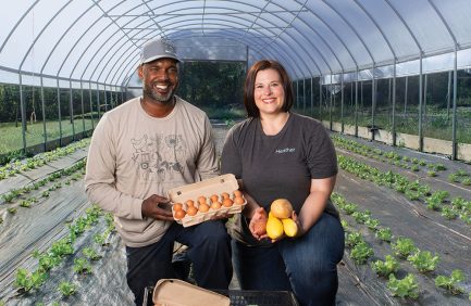 Travis Cleaver and Heather Cooper with a box of fresh vegetables and eggs from their Clev’s Family Market in Bonnieville.